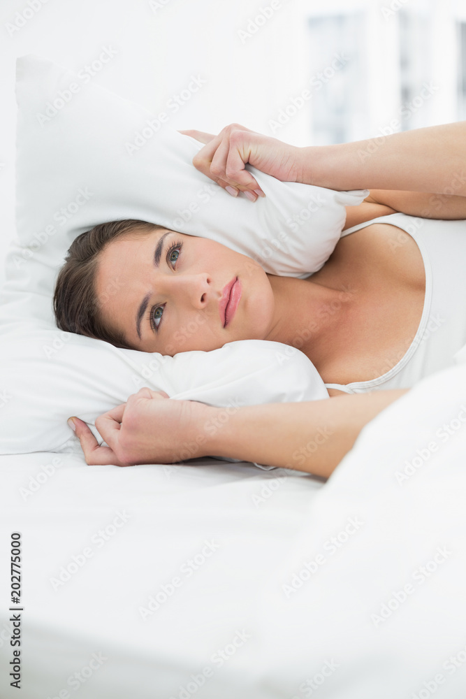 Woman covering ears with pillow in bed Woman covering ears with pillow in bed