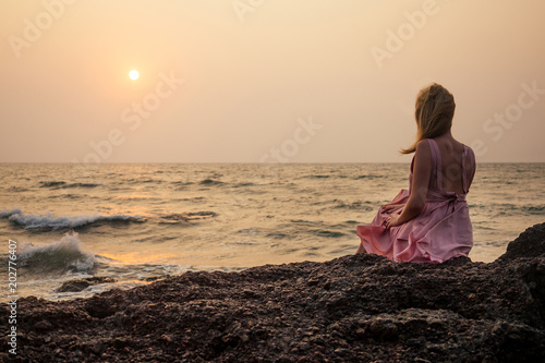 a woman is sitting and looking at the sunset on the beach © yurakrasil
