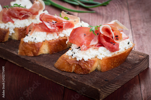 Baguette with cottage cheese, arugula and ham, sandwich on a board, selective focus. Wooden rustic background. Top view