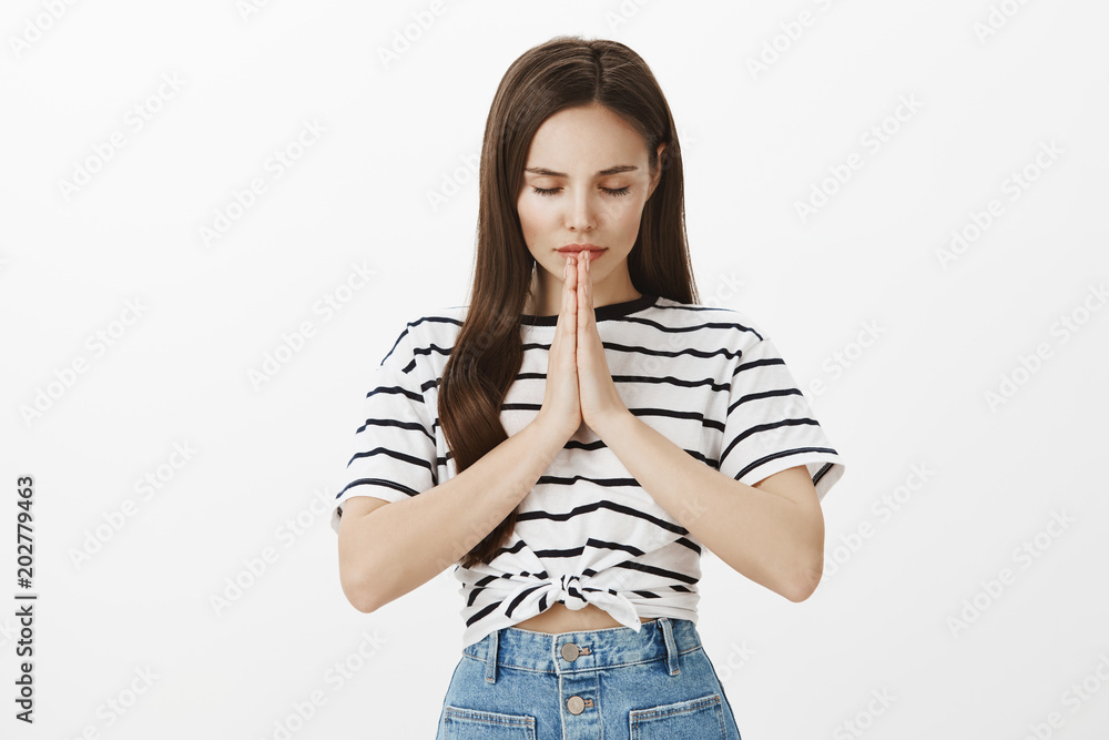 Getting concentration from space. Portrait of good-looking young european female, holding hands in pray and bowing head with closed eyes, focused on praying or wishing over white background Getting concentration from space. Portrait of good-looking young european female, holding hands in pray and bowing head with closed eyes, focused on praying or wishing over white background