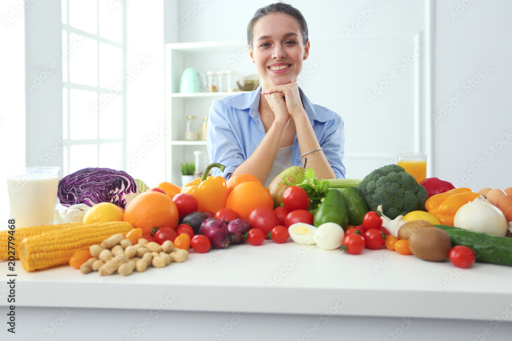 Young and cute woman sitting at the table full of fruits and vegetables in the wooden interior Young and cute woman sitting at the table full of fruits and vegetables in the wooden interior