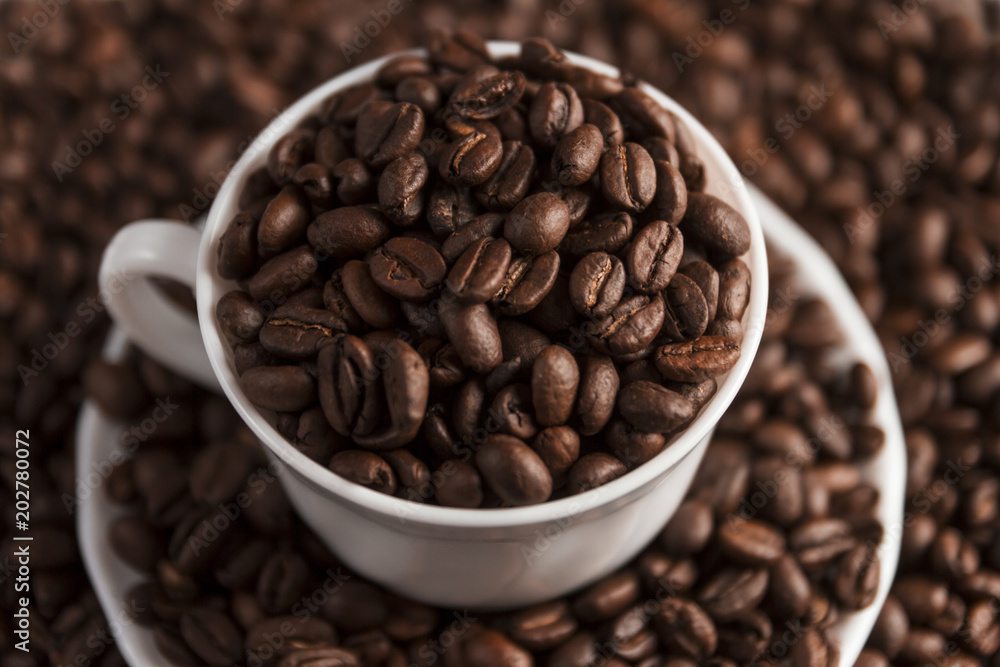 Fototapeta premium Cup filled with coffee beans on coffee beans background. Selective focus.