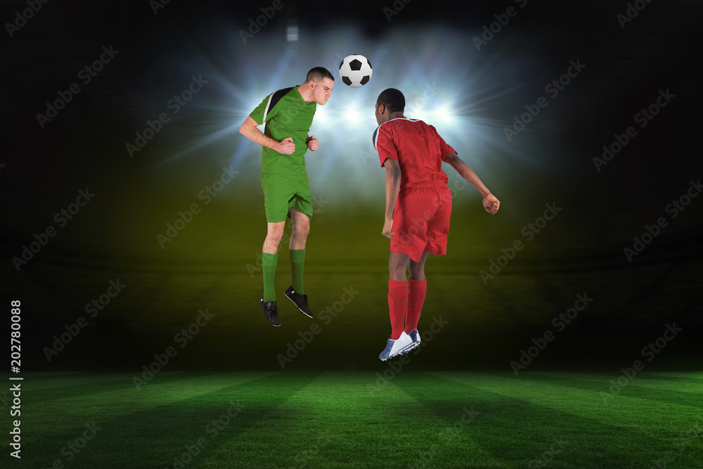 Football players tackling for the ball against football pitch under spotlights Football players tackling for the ball against football pitch under spotlights
