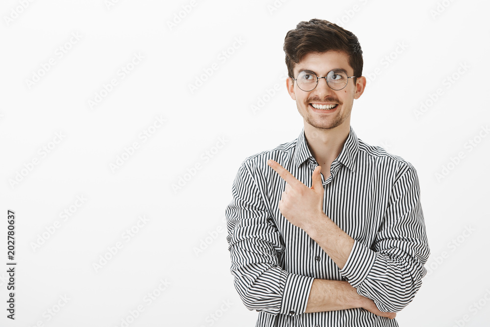 Guy recalled funny moment. Portrait of interested good-looking european male freelancer in glasses, pointing at upper left corner and smiling broadly, thinking about joke, standing over gray wall Guy recalled funny moment. Portrait of interested good-looking european male freelancer in glasses, pointing at upper left corner and smiling broadly, thinking about joke, standing over gray wall