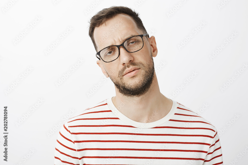 Obraz premium Indoor shot of unfocused sleepy male model in black glasses, squinting and being tired, having no idea what is happening, standing exhausted and not concentrated over gray background