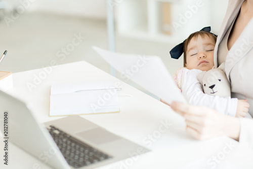Cute sleeping baby girl with teddybear on her business mother hands spending day in office