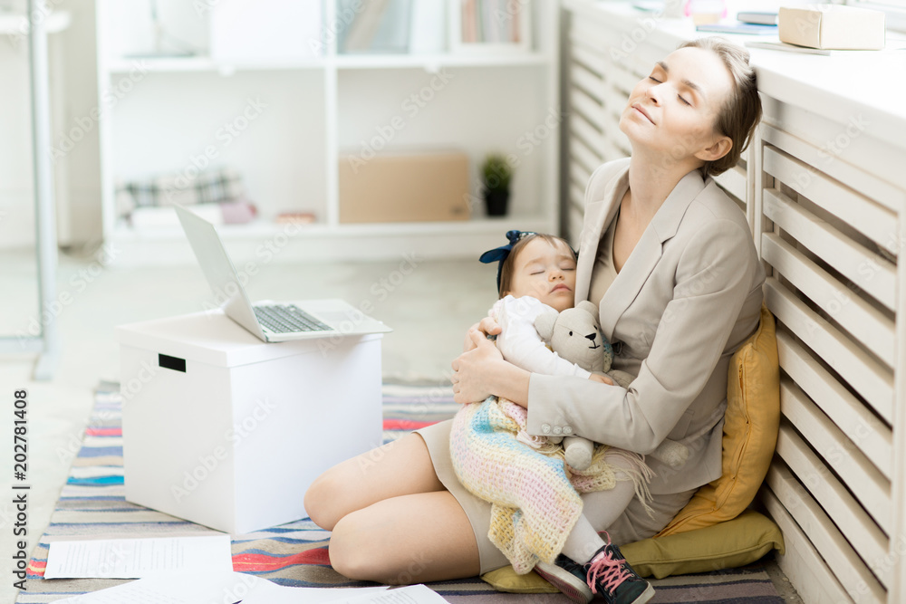 Φωτογραφία Tranquil young businesswoman with sleeping baby in her arms sitting on the floor