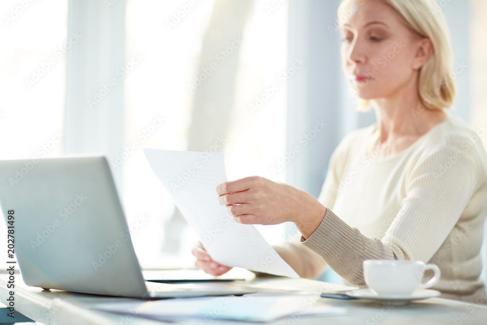 Professional accountant reading financial papers in front of laptop during working day Professional accountant reading financial papers in front of laptop during working day