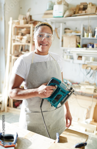 Foto Female carpenter with electric fretsaw looking at camera through protective eyeg