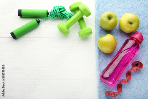 Pink bottle, green apple, dumbbells and skipping rope on white table