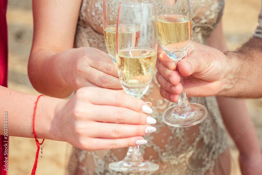 a group of young people celebrating with glasses of champagne on the beach. Glass glasses with sparkling wine in the hands of women and men on vacation a group of young people celebrating with glasses of champagne on the beach. Glass glasses with sparkling wine in the hands of women and men on vacation