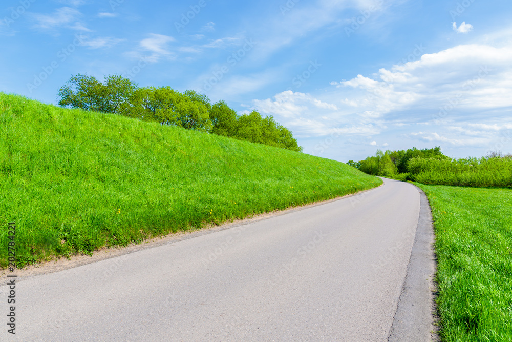 Rural road along Vistula river among green fields near Krakow city during spring season, Poland
