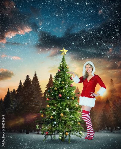 Pretty girl presenting in santa outfit against fir tree forest in snowy landscape