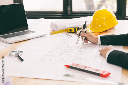 Architect hands working on blueprint plans with a pencil, a ruler, calculator, smartphone, laptop and engineering tools