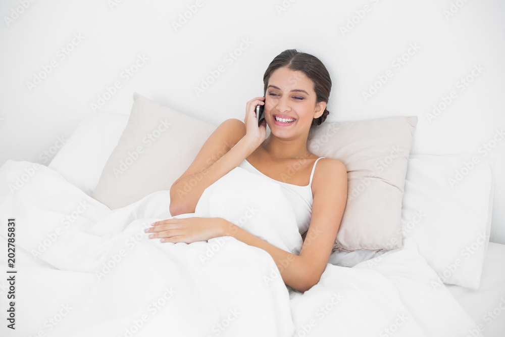 Laughing young brown haired model in white pajamas calling with her mobile phone Laughing young brown haired model in white pajamas calling with her mobile phone