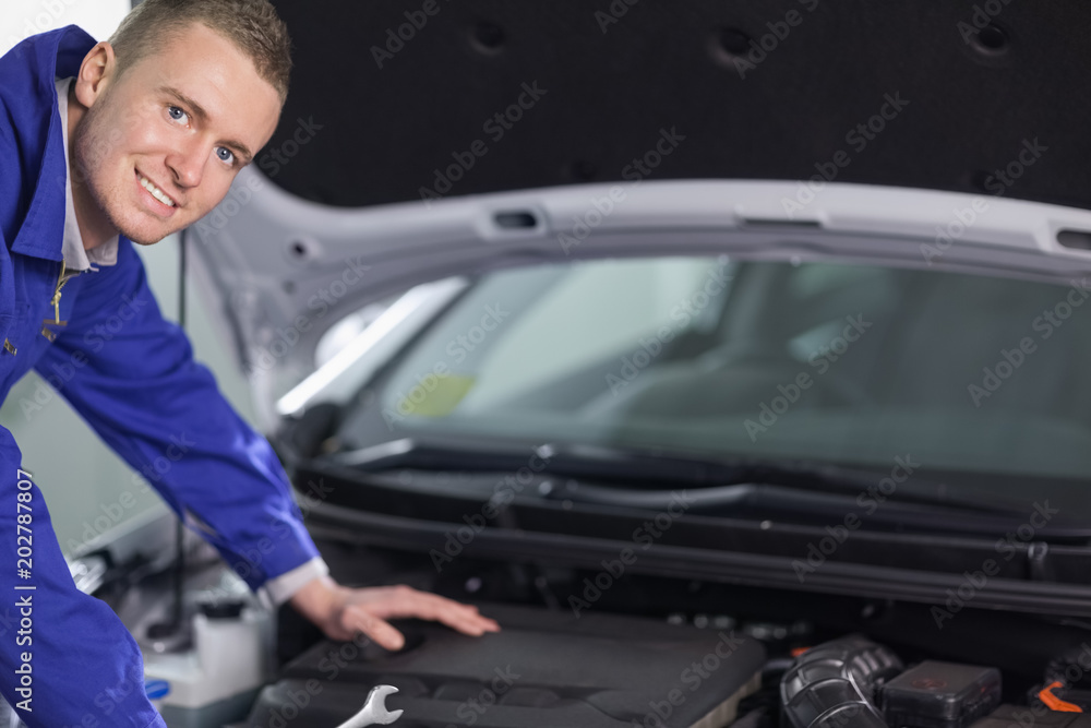 Mechanic looking at camera while leaning on a car
