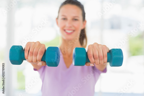 Smiling woman lifting dumbbell weights in a bright gym
