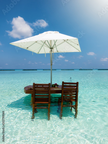 Fototapeta Naklejka Na Ścianę i Meble -  Tisch mit Sonnenschirm und Stühlen in türkisen, tropischen Gewässern