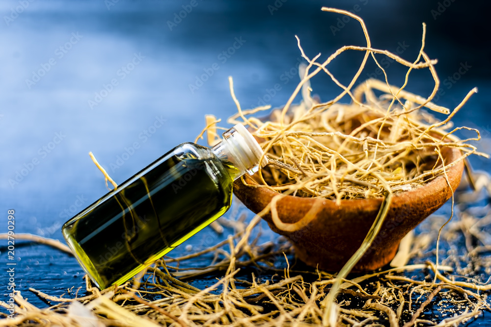 Φωτογραφία Floral and ayurvedic essence of herb Vetiver grass or Khus in a transparent bottle used in many beverages of Indian and Asia with dried vetiver grass in a clay bowl on black surface