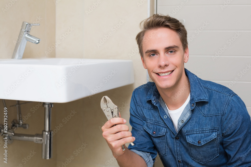 Smiling plumber with wrench by sink in bathroom Smiling plumber with wrench by sink in bathroom