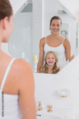 Happy mother and daughter looking at bathroom mirror