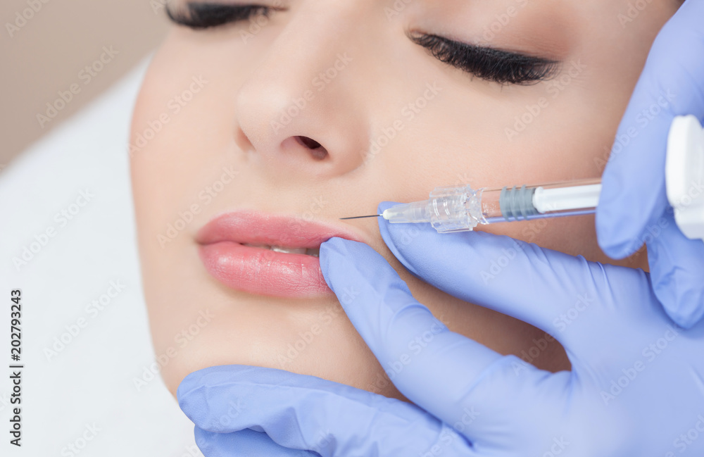 The doctor cosmetologist makes Lip augmentation procedure of a beautiful woman in a beauty salon.Cosmetology skin care. The doctor cosmetologist makes Lip augmentation procedure of a beautiful woman in a beauty salon.Cosmetology skin care.