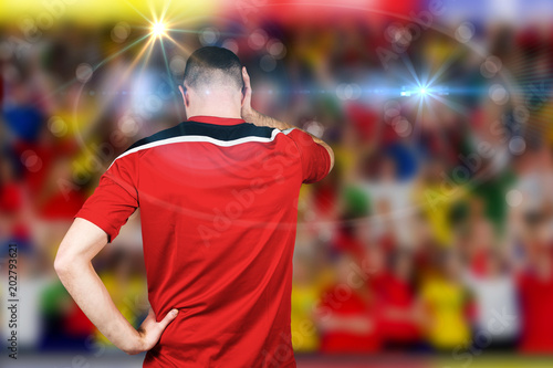 Disappointed football player looking down against blurry football pitch with crowd