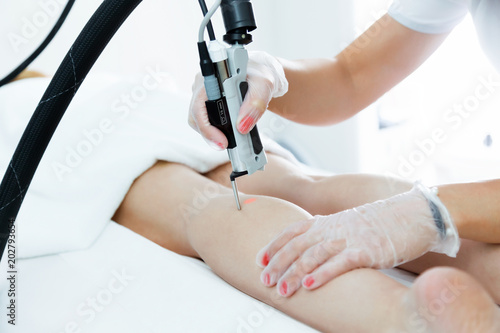 The beautician's hands removing leg hair with a laser to her client in the beauty salon.