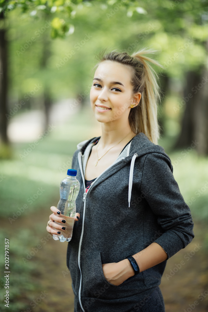 Thirsty woman drinking water to recuperate after jogging in city park Thirsty woman drinking water to recuperate after jogging in city park