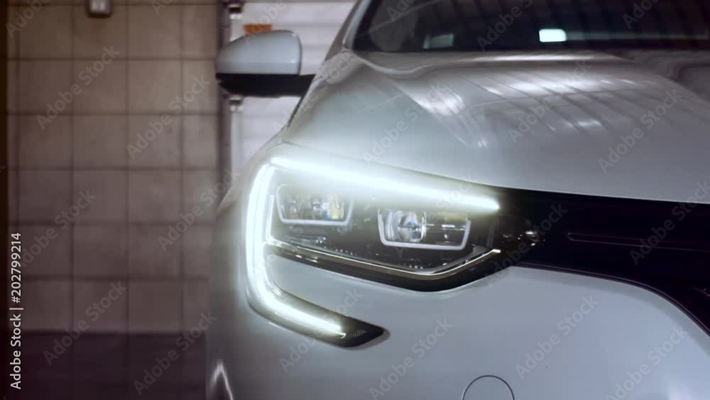 A white car with lights on is in the garage. Car service. Xenon. 4k. A white car with lights on is in the garage. Car service. Xenon. 4k.