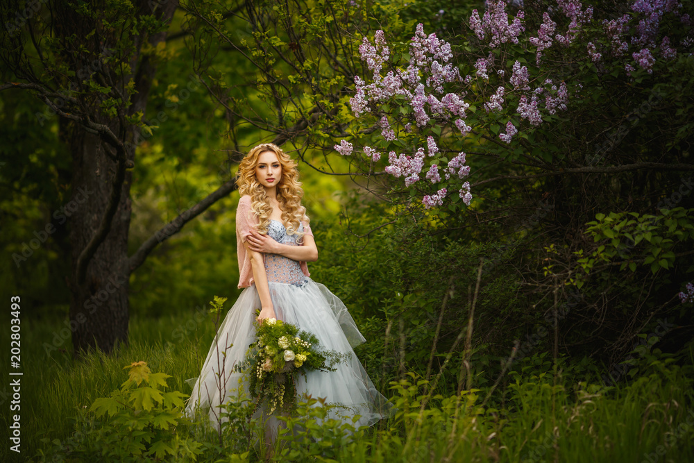 Handsome young woman in grey dress on lilac bushes background.