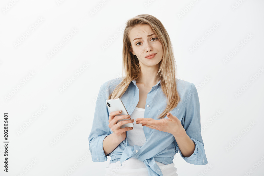 Waist-up shot of annoyed unimpressed attractive european girlfriend with fair hair, smirking, holding smartphone and pointing at device with palm, being shocked with stupid message of ex-boyfriend Waist-up shot of annoyed unimpressed attractive european girlfriend with fair hair, smirking, holding smartphone and pointing at device with palm, being shocked with stupid message of ex-boyfriend