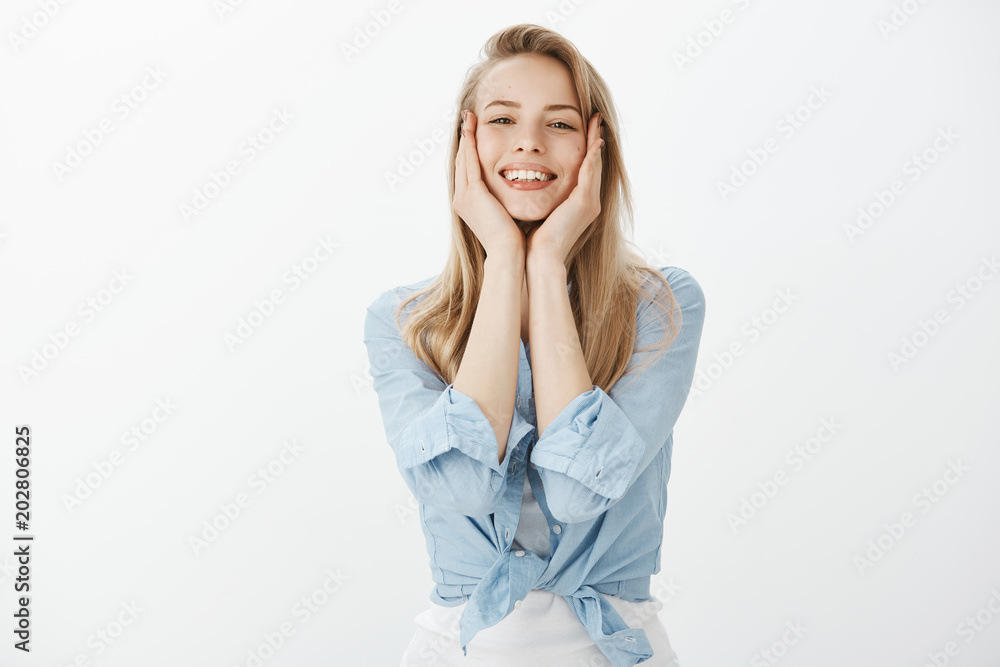Good-looking cute female student in stylish outfit, touching face with palms gently and smiling broadly, being satisfied with result of facial mask, feeling relieved while standing over white wall Good-looking cute female student in stylish outfit, touching face with palms gently and smiling broadly, being satisfied with result of facial mask, feeling relieved while standing over white wall