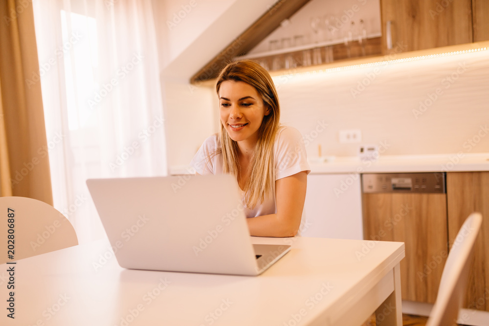 Beautiful young girl, casually dressed is working on her laptop in the living room Beautiful young girl, casually dressed is working on her laptop in the living room