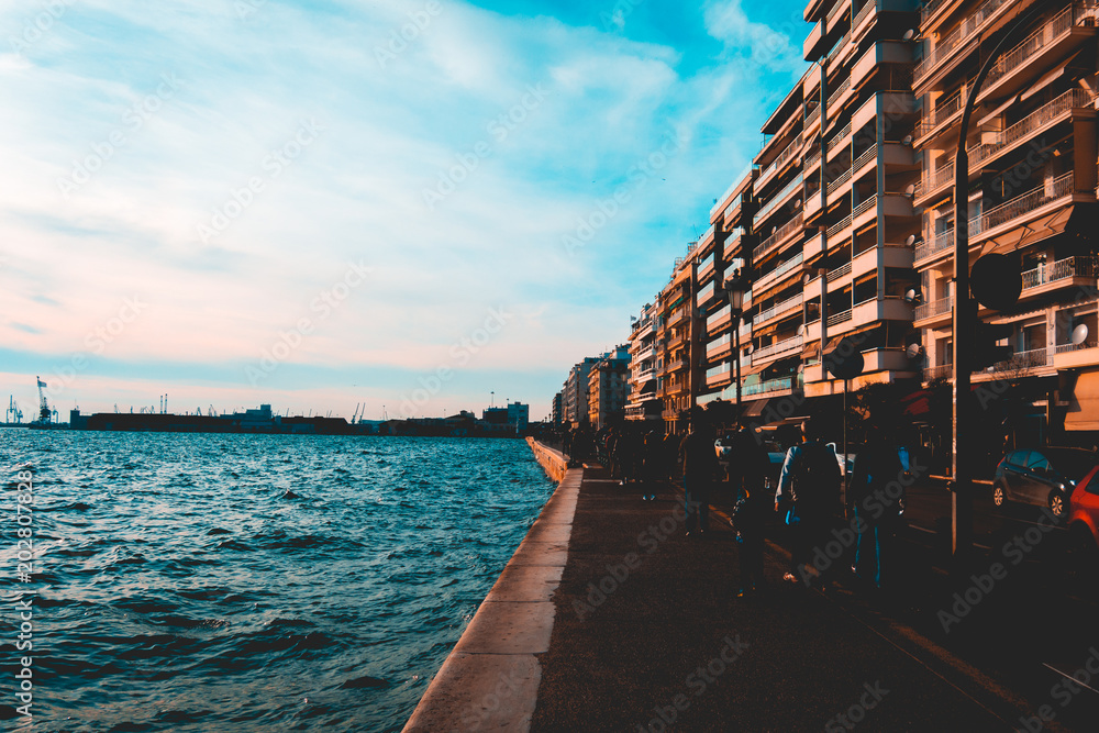 Fototapeta premium promenade of thessaloniki with darken tourist sillhouetts and port in the background