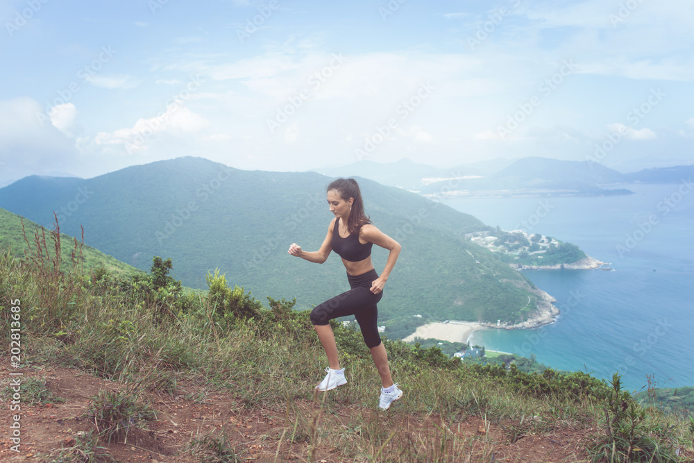 Fitness female athlete wearing black sportswear doing cardio exercise, running in mountains with inspirational sea view