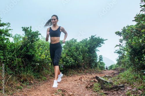 Fitness female athlete running on forest path in mountainous area in summer. Sporty woman working out going uphill.