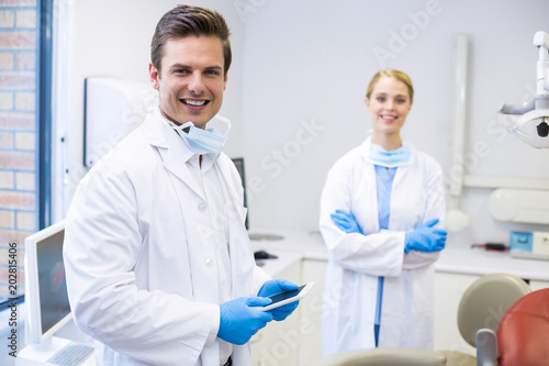 Portrait of dentist holding digital tablet while his colleague in background