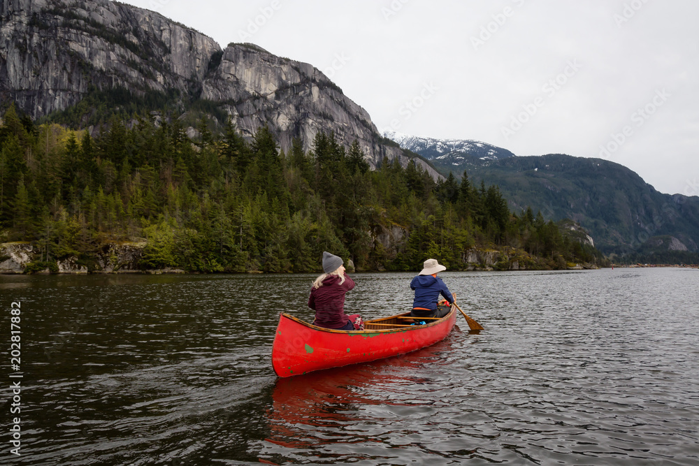 Adventurous people on a wooden canoe are paddling in a river with beautiful rocky mountain in the background. Taken in Squamish, North of Vancouver, BC, Canada.