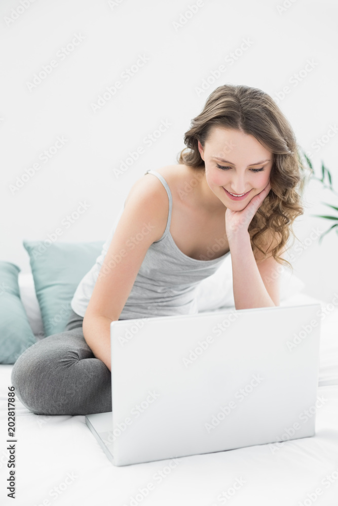 Smiling casual brunette using laptop in bed Smiling casual brunette using laptop in bed