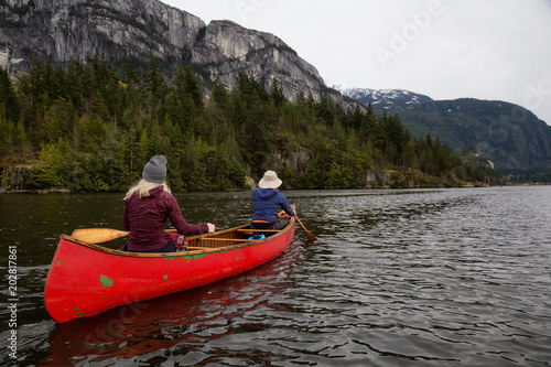 Adventurous people on a wooden canoe are paddling in a river with beautiful rocky mountain in the background. Taken in Squamish  North of Vancouver  BC  Canada.
