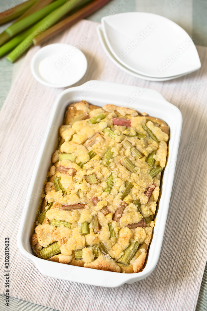 Freshly baked rhubarb crumble cake in baking dish, photographed with natural light (Selective Focus, Focus in the middle of the cake)