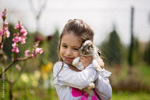 Little girl playing with white rabbit in park on a sunny summer day