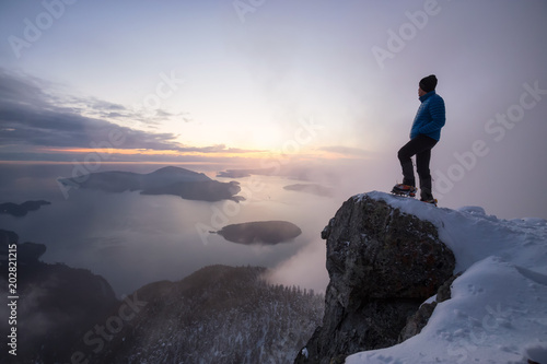 Adventurous man standing on the side of a steep cliff during a beautiful vibrant sunset. Taken on top of St Mark s Peak  North of Vancouver  BC  Canada.