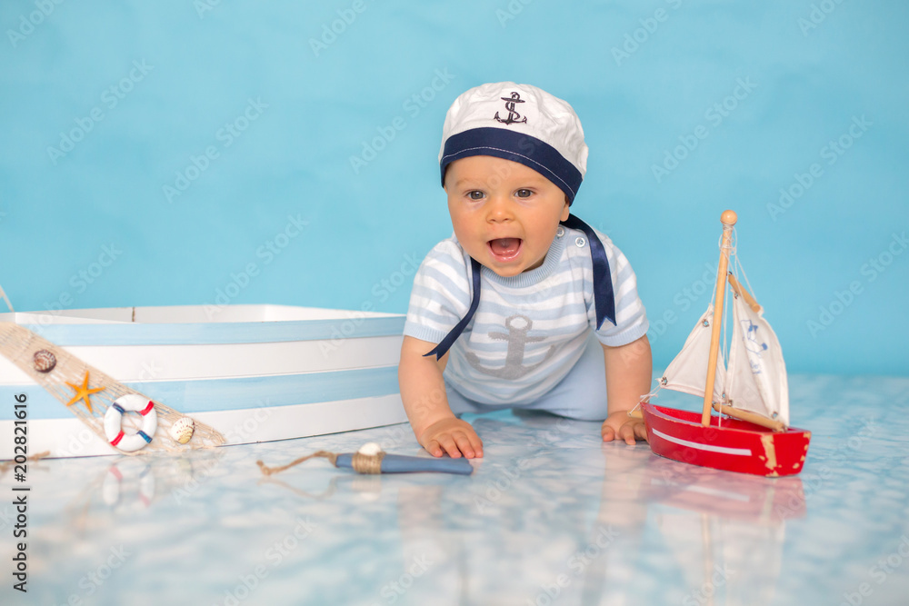 Cute toddler baby boy in wooden boat, playing with fishes, starfish and binoculars as sailman