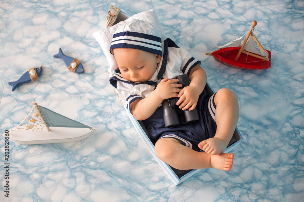 Φωτογραφία Cute toddler baby boy sleeping in wooden boat with fishes, starfish and binocula