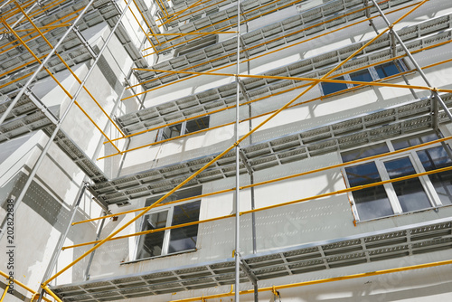 scaffolding near a new house  building exterior  construction and repair industry  white wall and window  yellow pipe