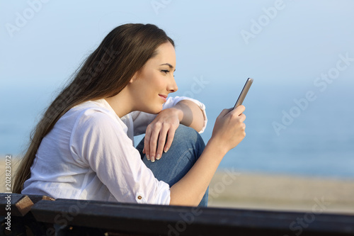Relaxed girl watching phone content on the beach
