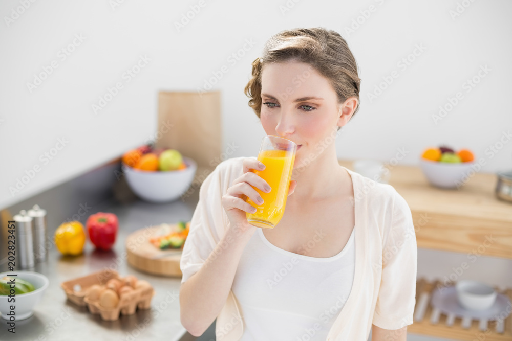 Lovely brunette woman drinking a glass of orange juice standing in her kitchen Lovely brunette woman drinking a glass of orange juice standing in her kitchen