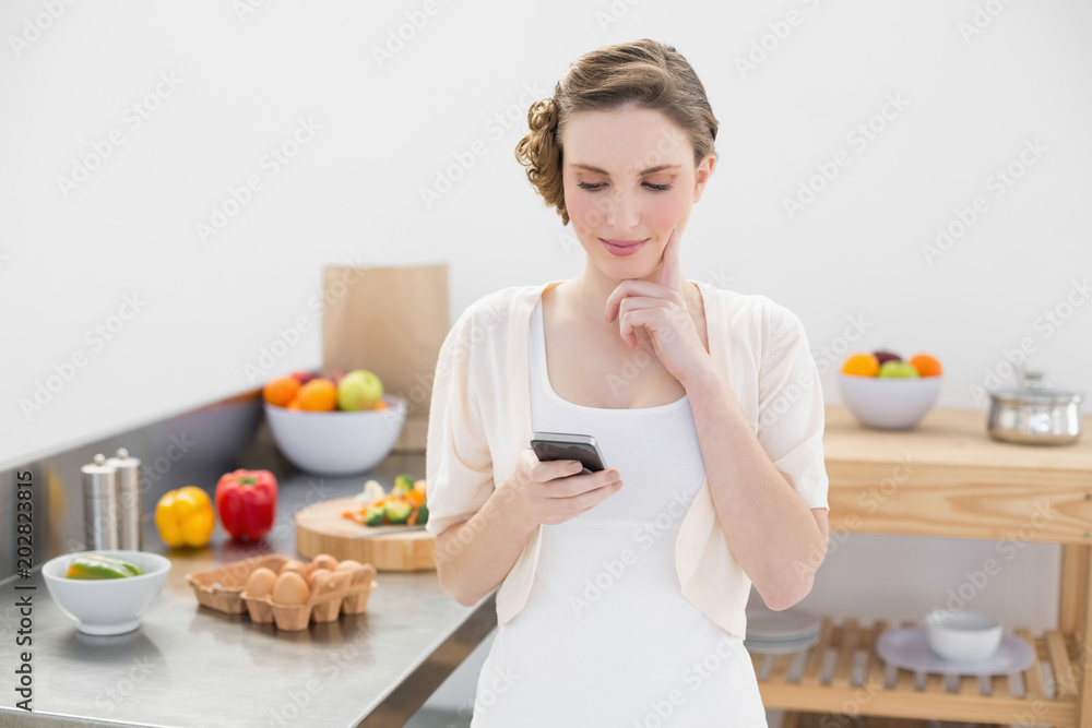 Thinking beautiful woman using her smartphone standing in the kitchen Thinking beautiful woman using her smartphone standing in the kitchen